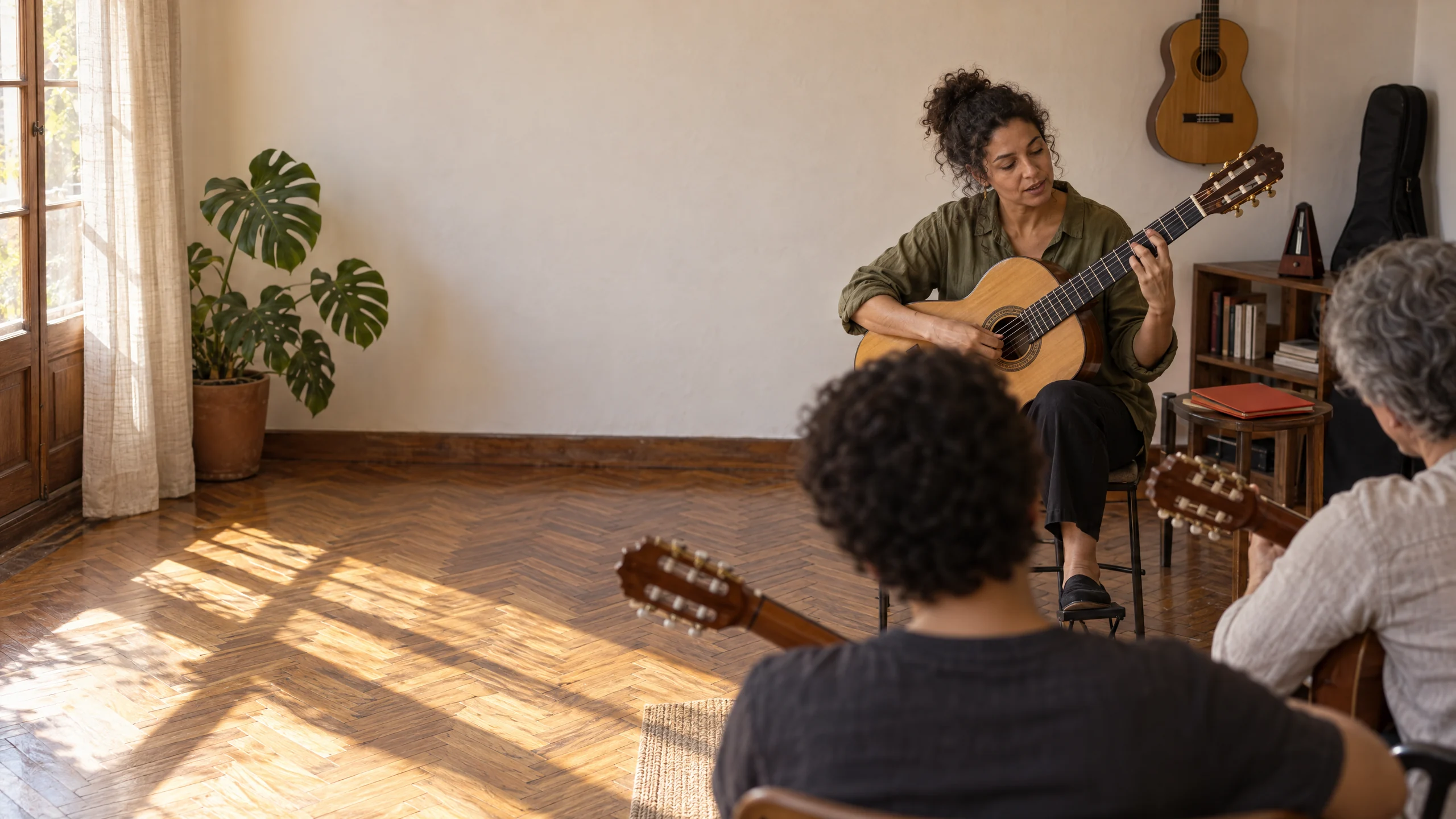 A guitar teacher playing the chord for her in-person class, with two students seen from behind, each holding their own guitar.
